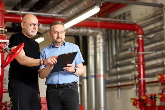 Das ist ein Bild des Teamleiters des technischen Gebäudemanagements mit einem Techniker in der Hauptsprinkleranlage in Gebäude 2 der Hochschule Düsseldorf. 