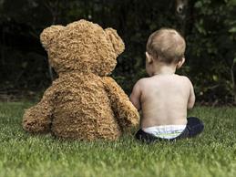A baby is sitting with his teddy on a meadow