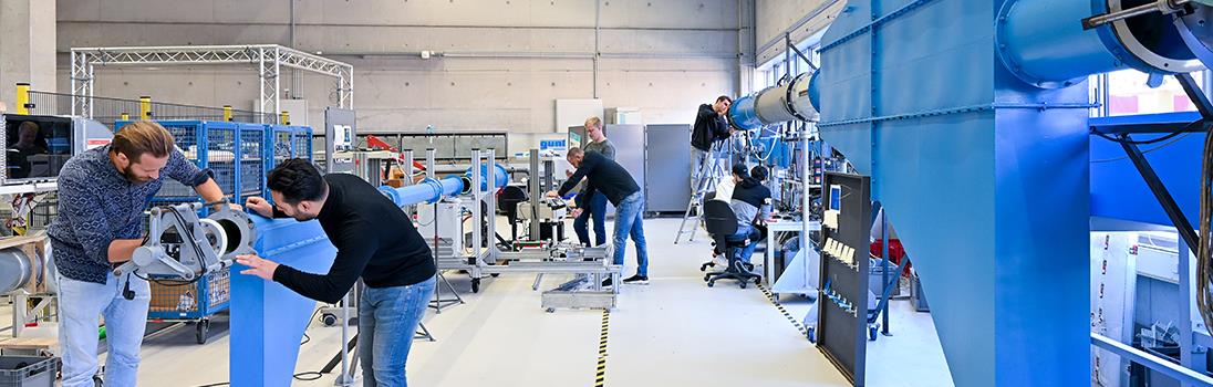 Mehrere männliche Studierende arbeiten in der Maschinenhalle der Hochschule an einem Großgerät.