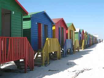 Fröhlich bunt gestrichene Holzhäuschen in allen Farben, wahrscheinlich Badekabinen, stehen nebeneinander gereiht am Strand von Muizenberg in der Nähe von Kapstadt