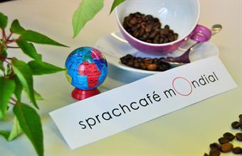 A smal colourful globe next to a pink cup, which is filled with coffee beans. Below it, the writing: Sprachcafé mOndial.